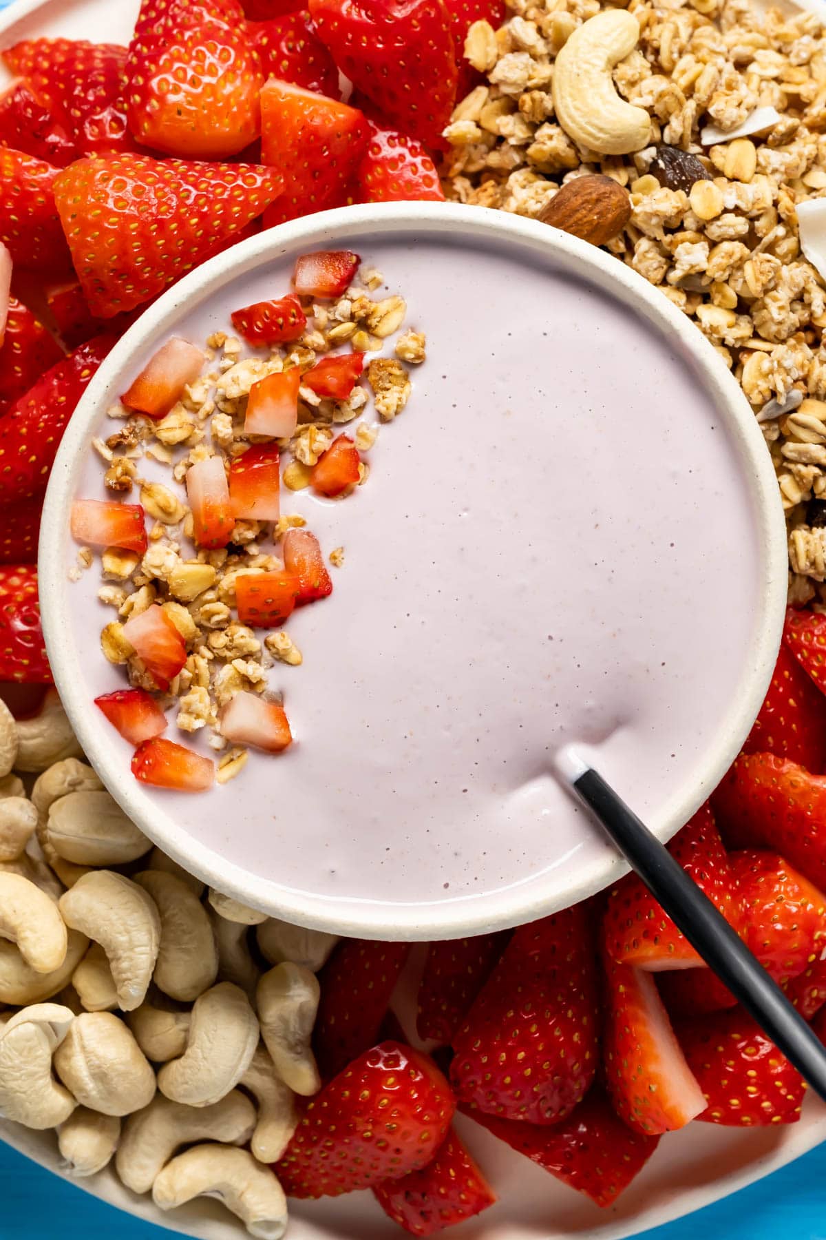 Vegan yogurt in a bowl topped with granola and sliced strawberries.