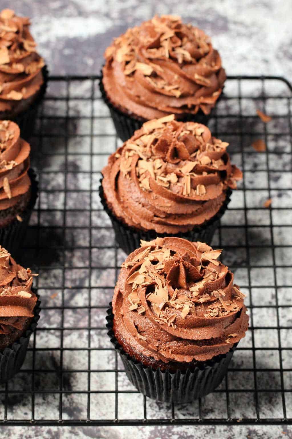 Classic vegan chocolate cupcakes topped with vegan chocolate buttercream and chocolate shavings on a wire cooling rack. 