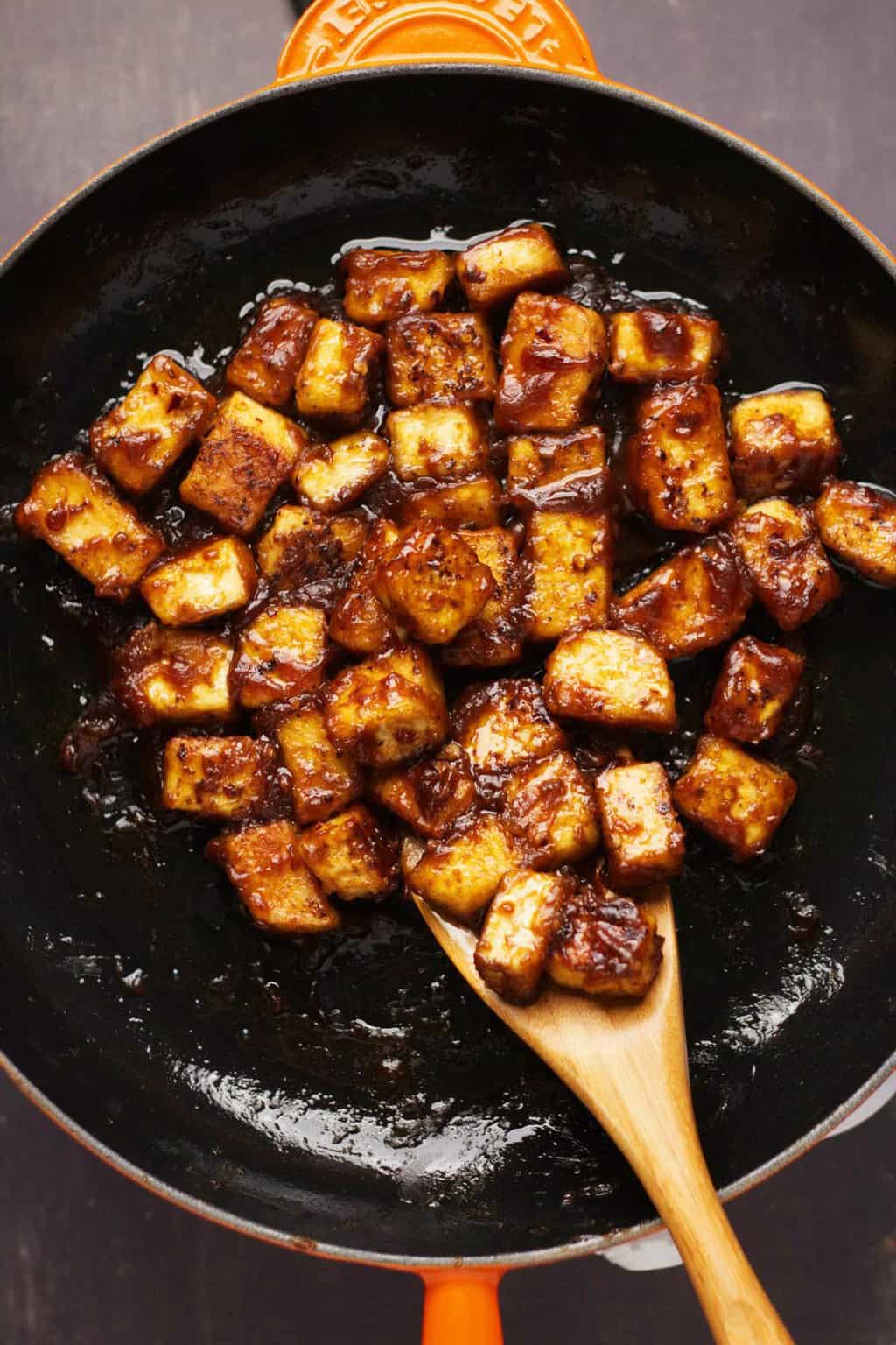 General Tso's tofu in a frying pan with a wooden spoon. 
