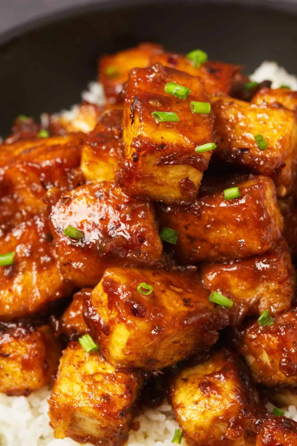 General Tso's tofu served with basmati rice and chopped chives in a black bowl. 