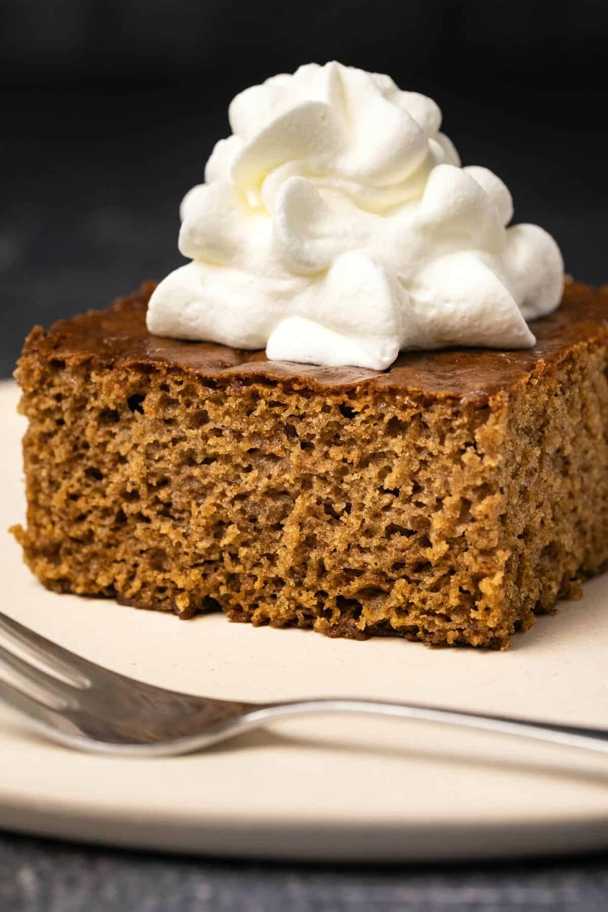 Slice of gingerbread with whipped cream on a white plate with a cake fork. 
