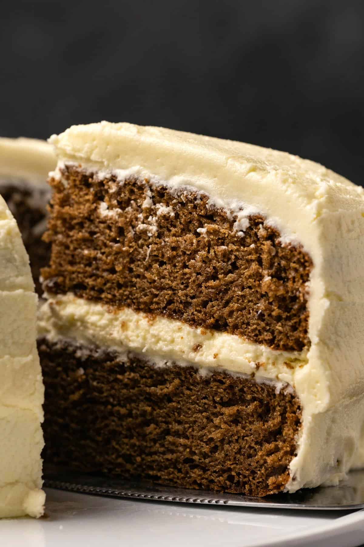 Vegan gingerbread cake on a white cake stand with one slice cut.