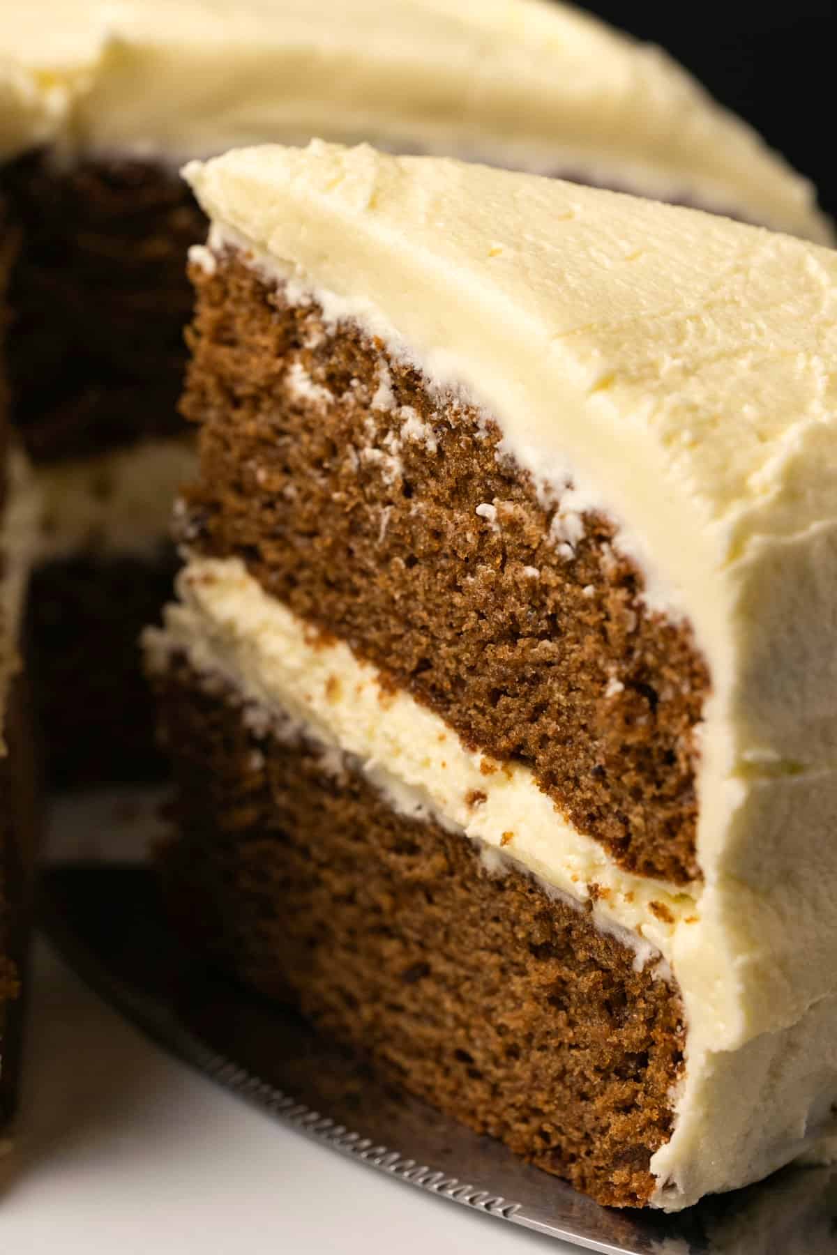Vegan gingerbread cake on a white cake stand with one slice cut and ready to serve. 