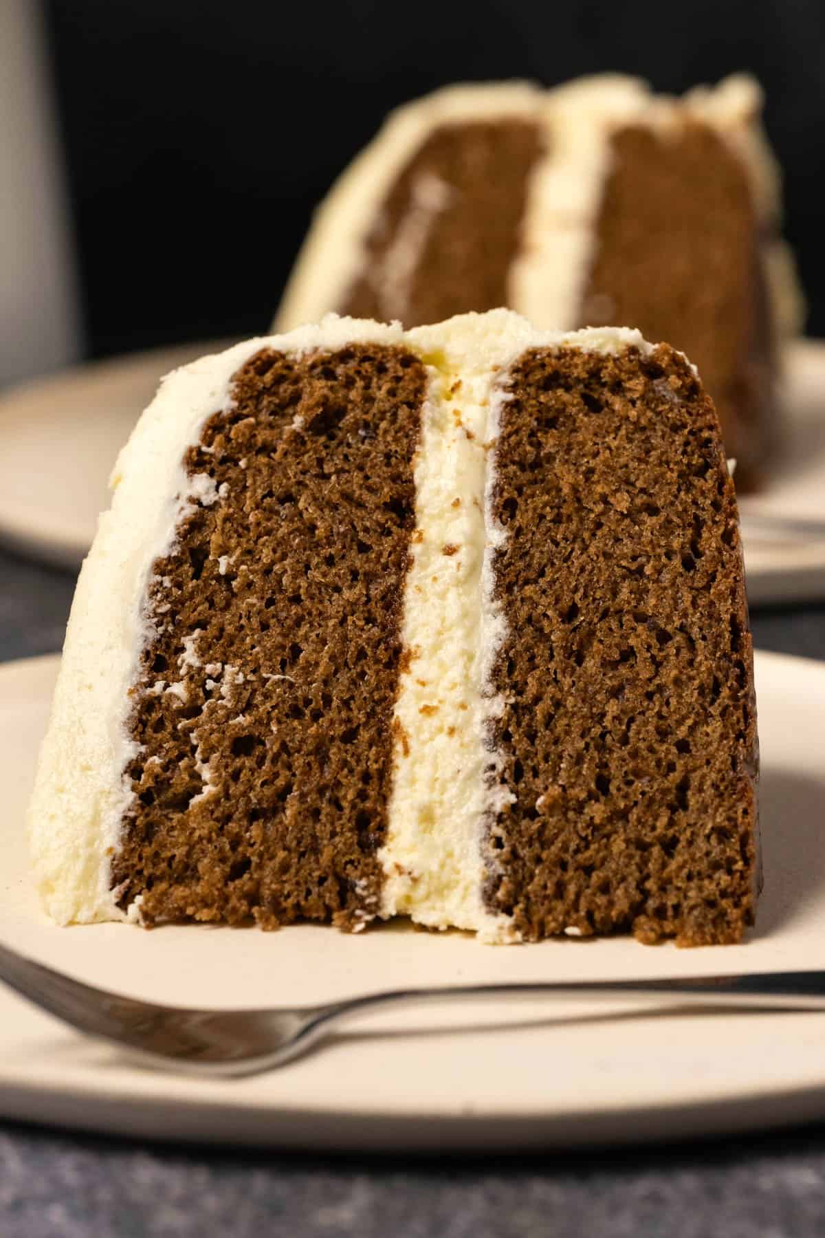Slice of frosted vegan gingerbread cake on a white plate. 