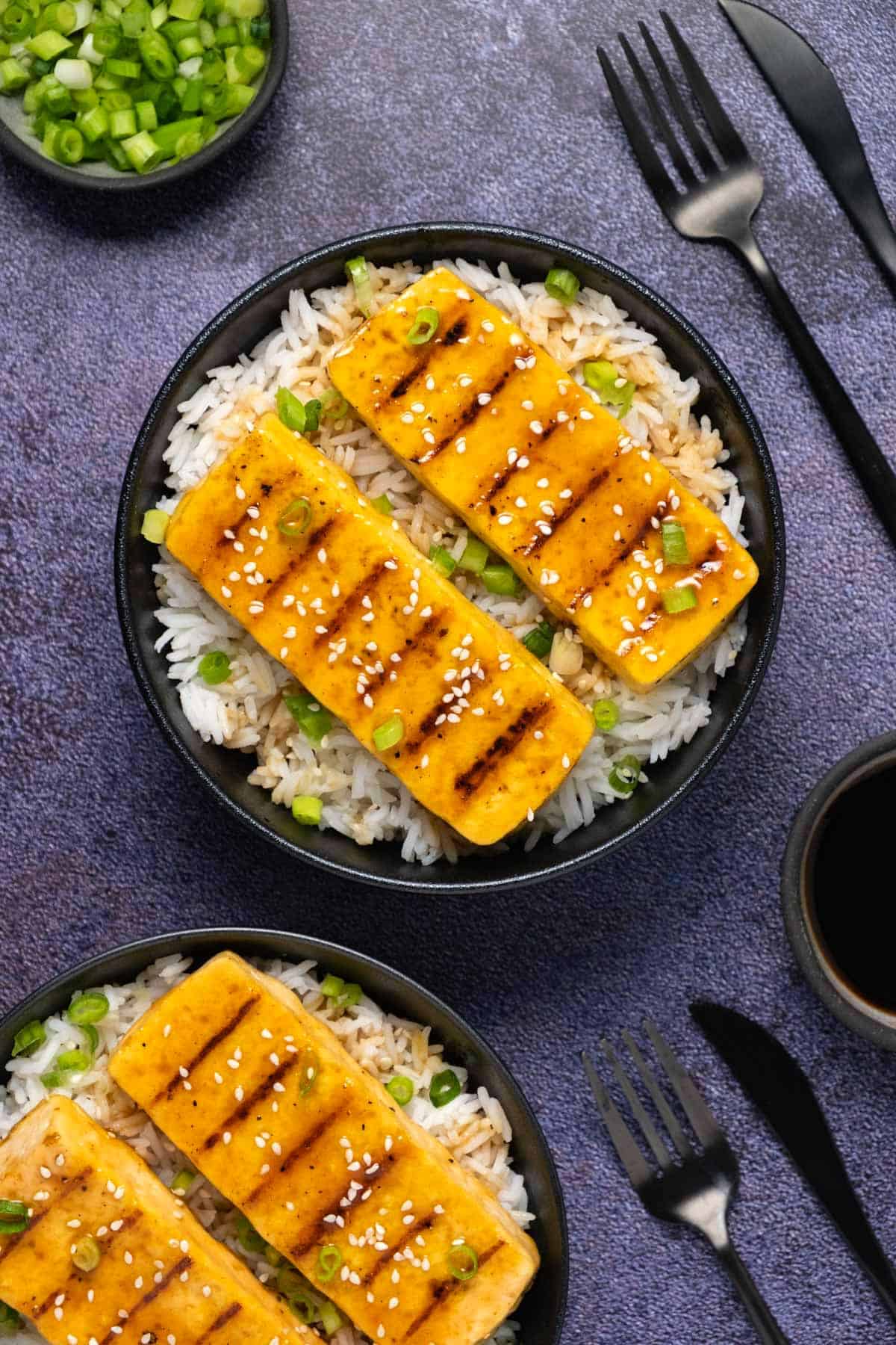Grilled tofu served with rice and chopped green onions in a black bowl. 