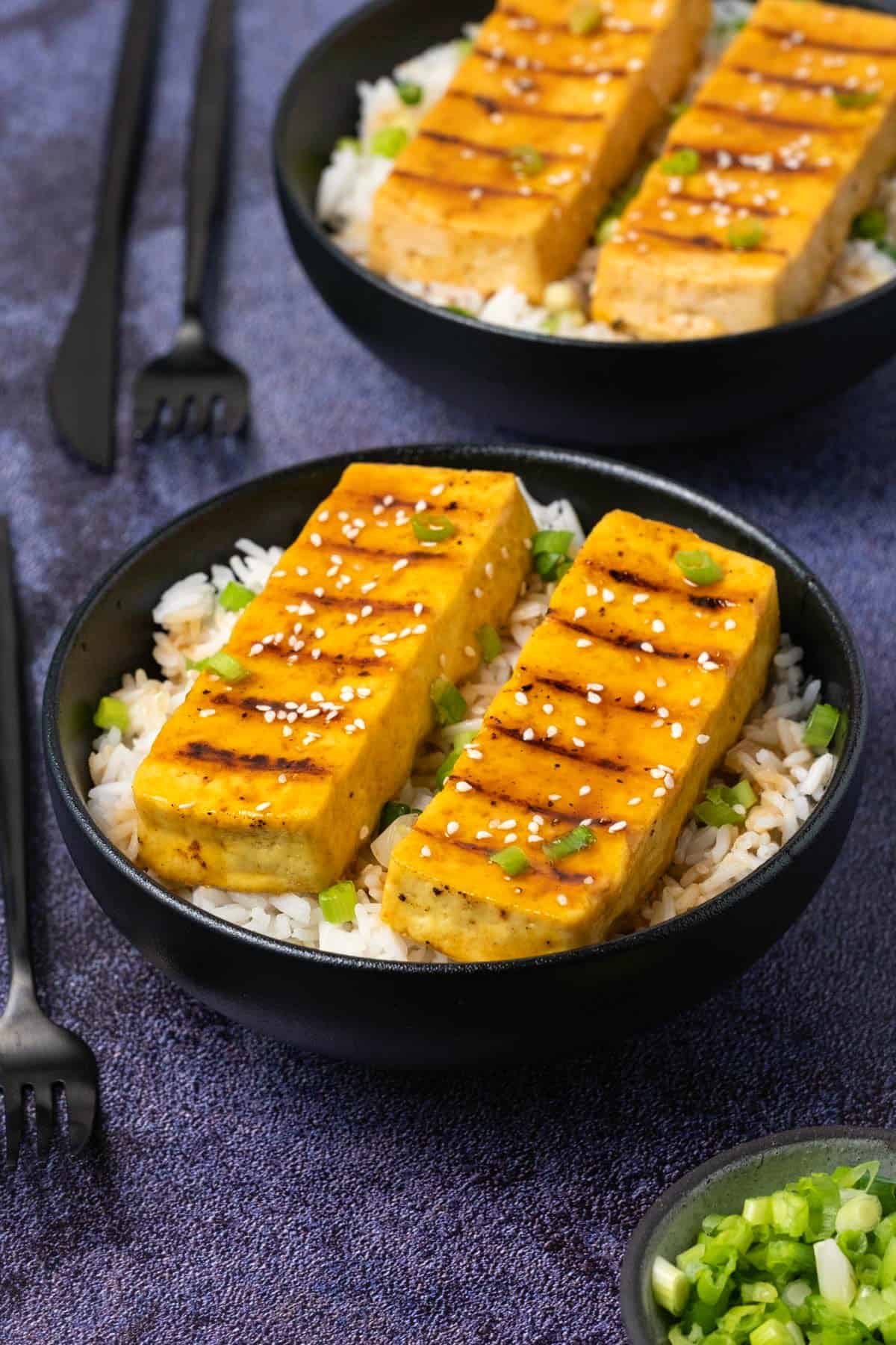 Grilled tofu with green onions and basmati rice in a black bowl. 