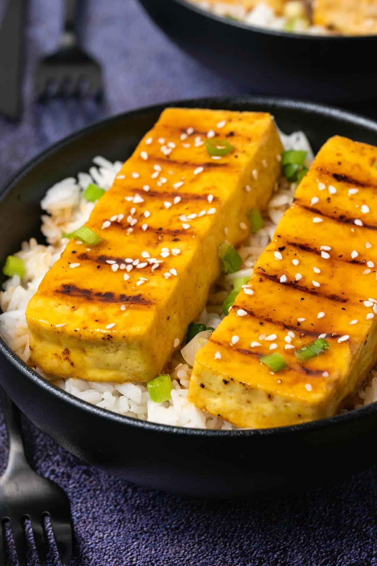 Grilled tofu with rice and green onions in a black bowl. 