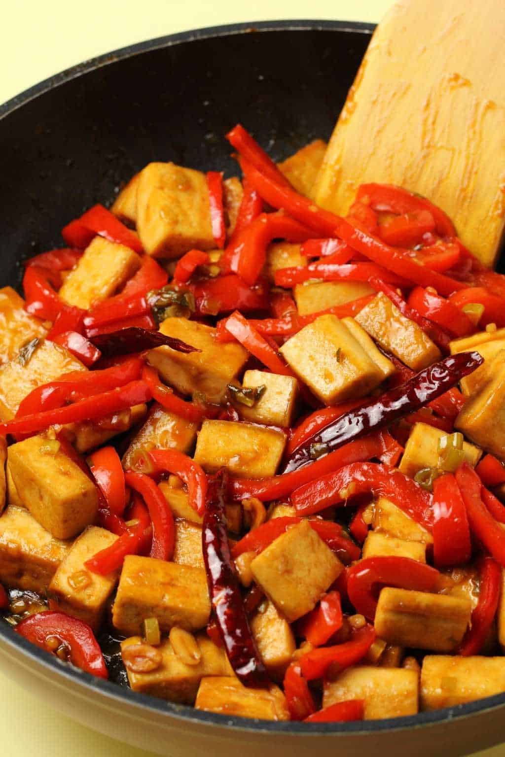 Kung pao tofu in a frying pan with a wooden spatula. 