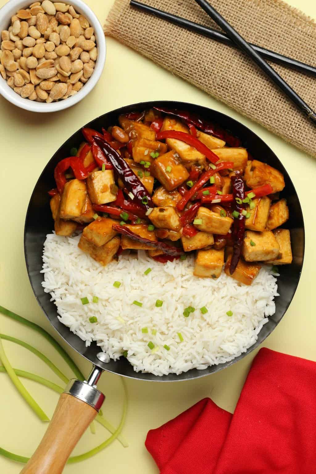 Kung pao tofu in a wok with rice and topped with chopped spring onions.