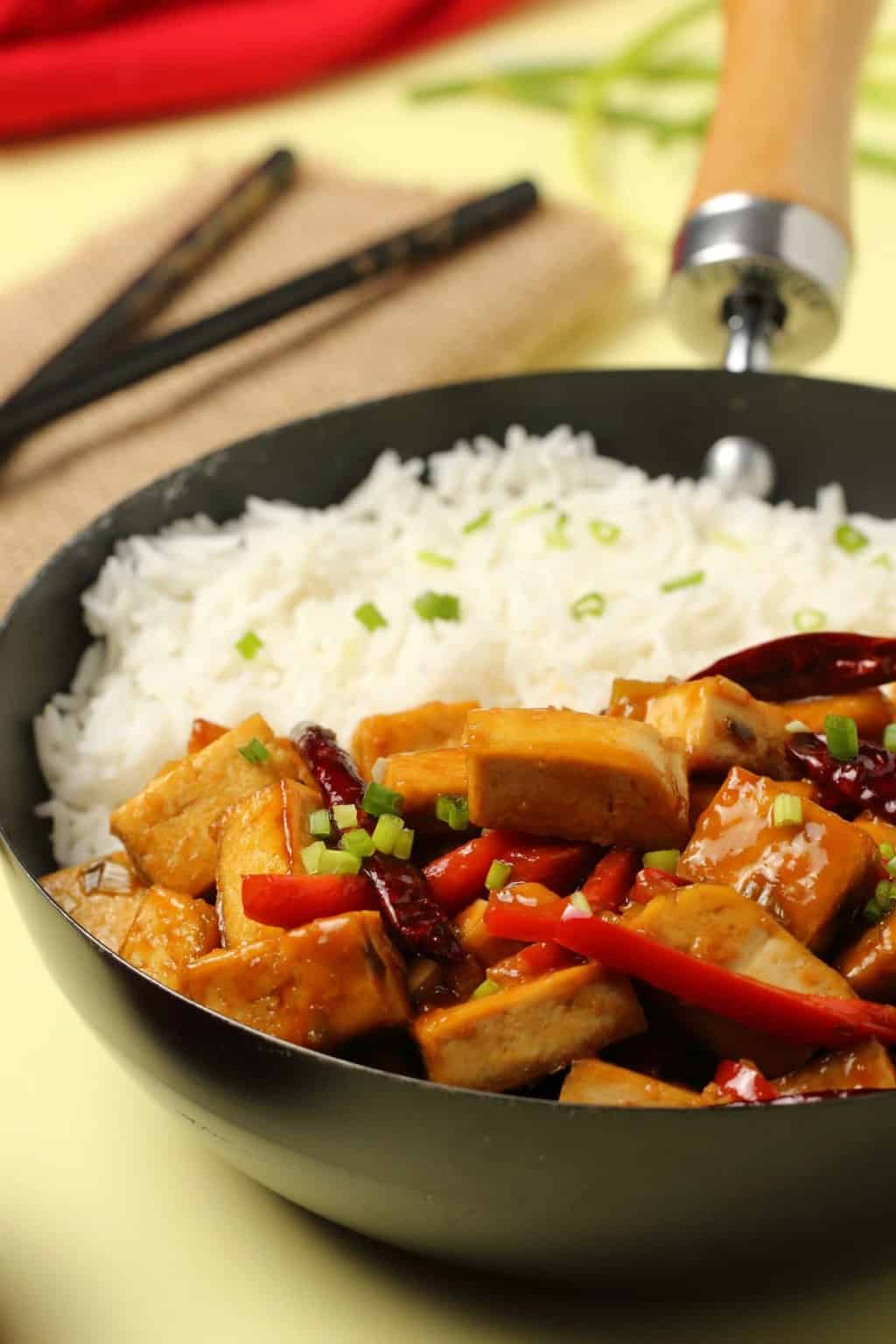 Kung pao tofu served in a wok with basmati rice and topped with chopped spring onions. 