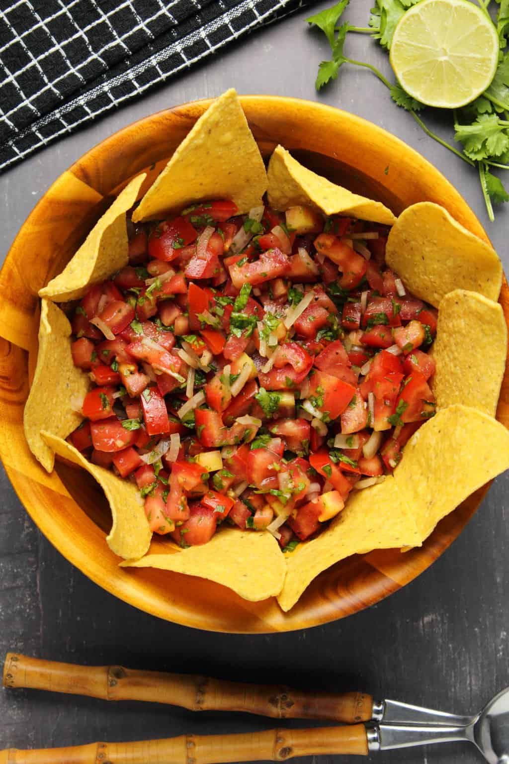 Pico de gallo in a wooden bowl surrounded by corn chips. 