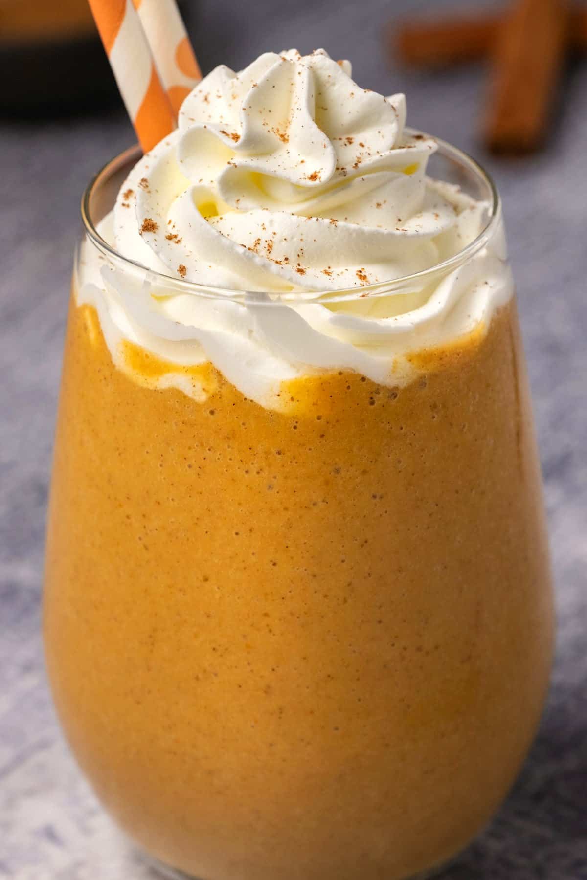 Pumpkin smoothie topped with whipped cream in a glass with two orange and white straws.