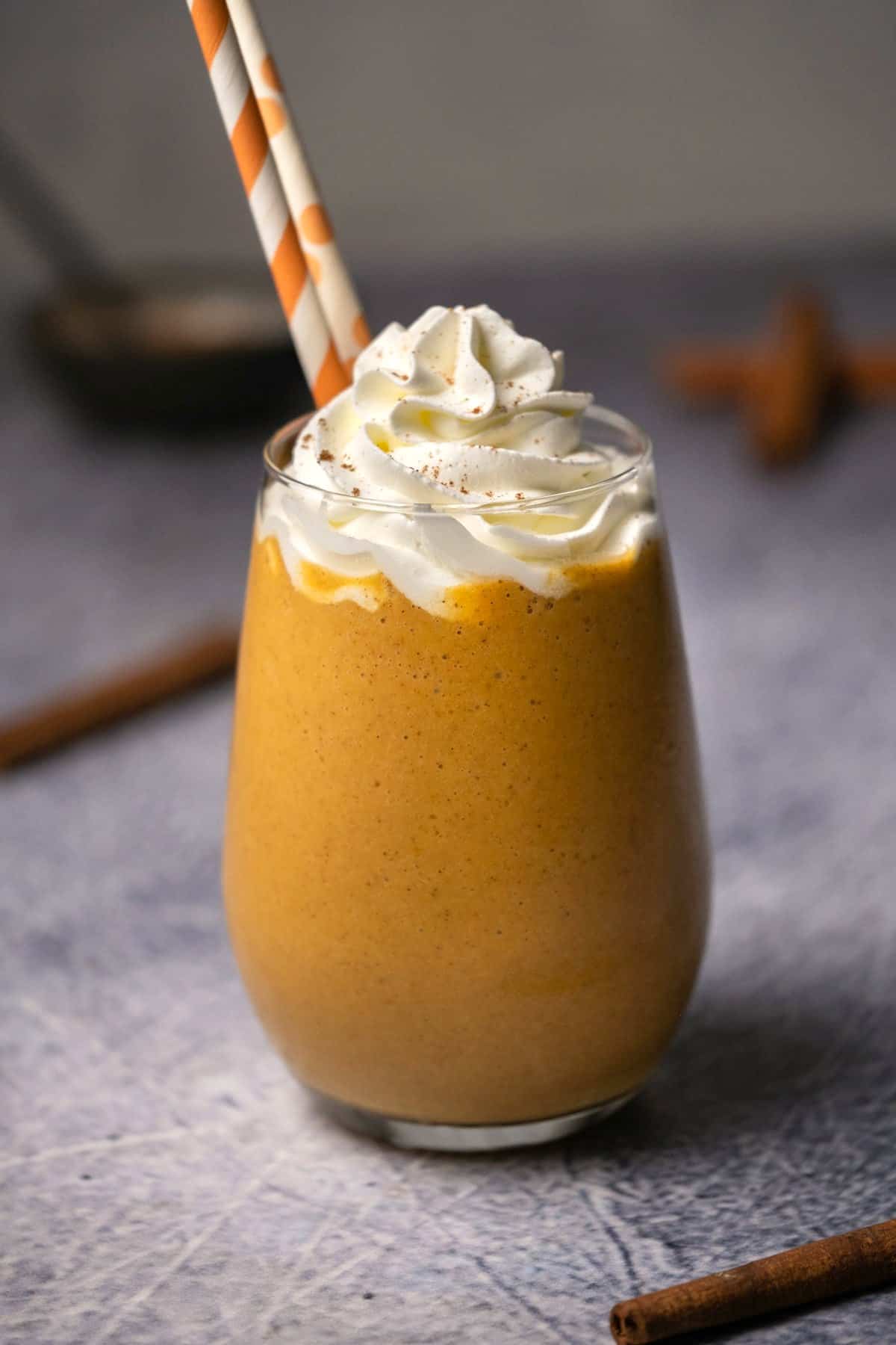 Pumpkin smoothie in a glass topped with whipped cream and pumpkin pie spice. 