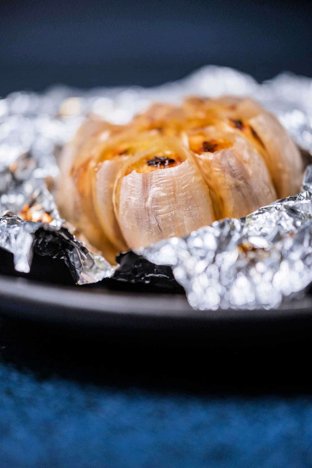 Whole roasted garlic on a black plate. 