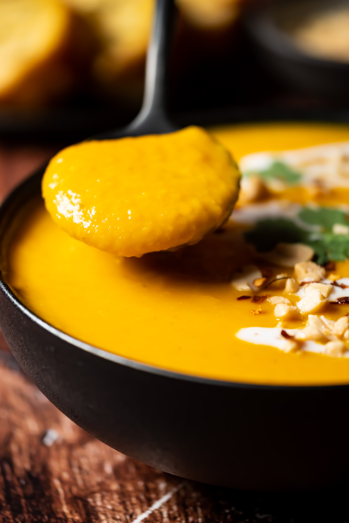 Thai butternut squash soup in a black bowl with a spoon.