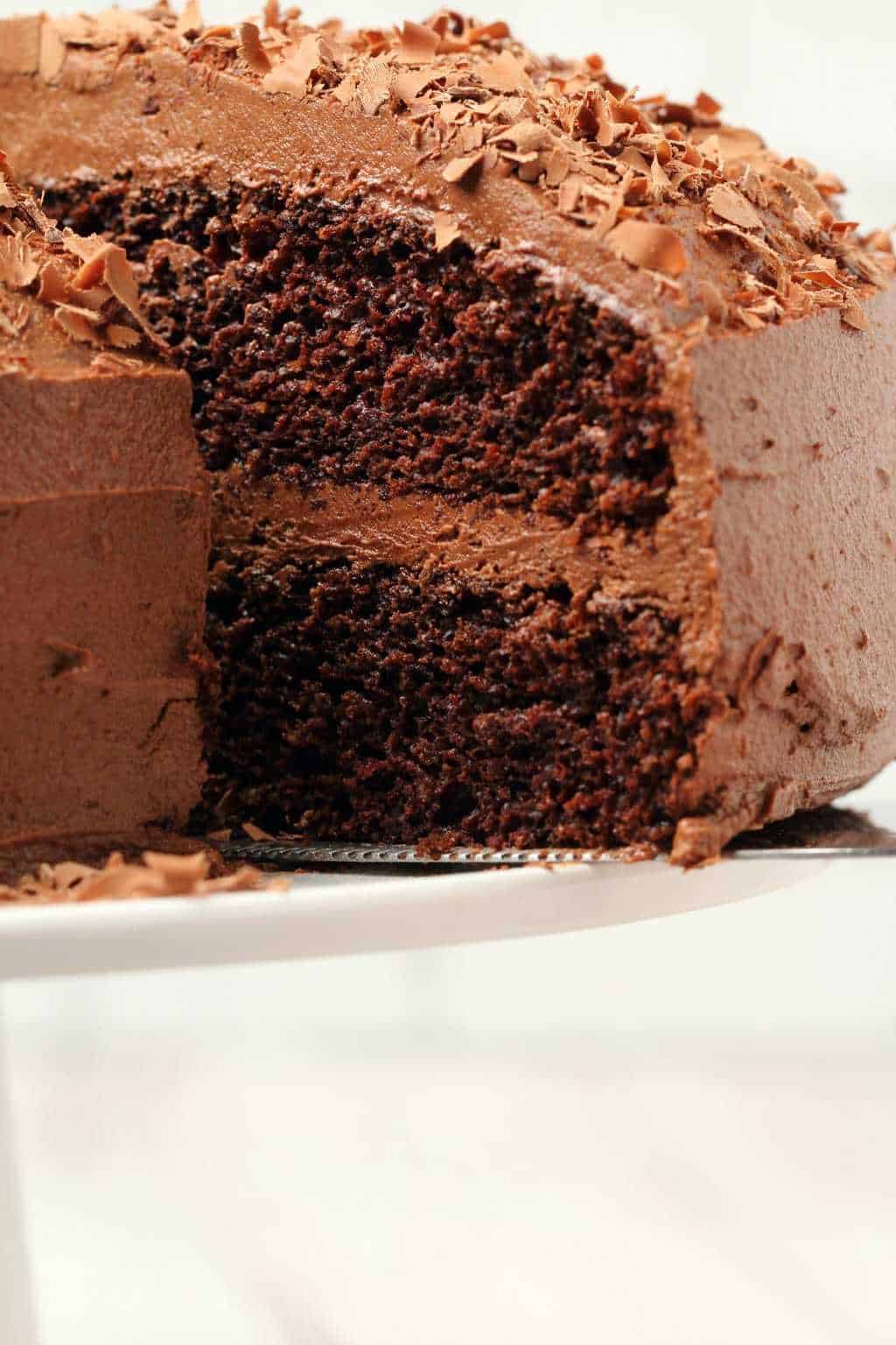 Chocolate cake with one slice cut and ready to serve on a white cake stand. 