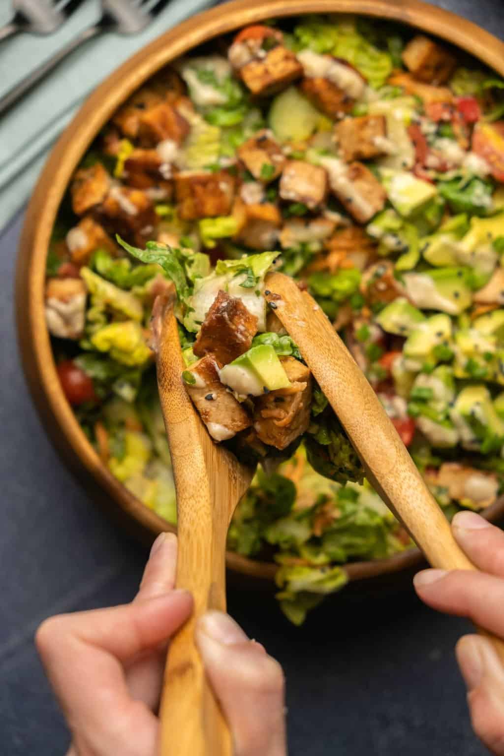 Dishing up tofu salad from a wooden bowl with wooden salad spoons. 
