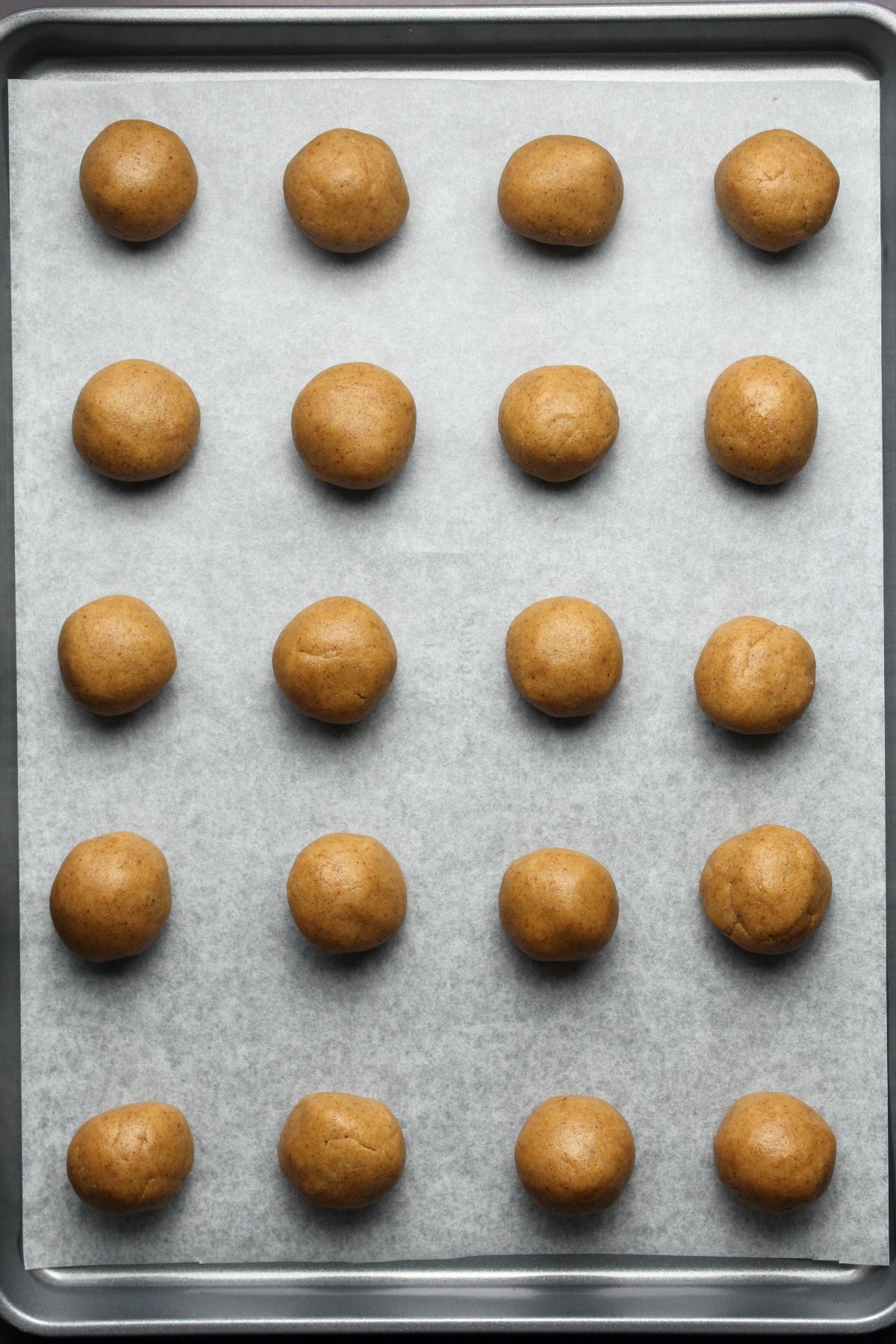Almond butter cookie dough rolled into balls on a parchment lined baking tray.