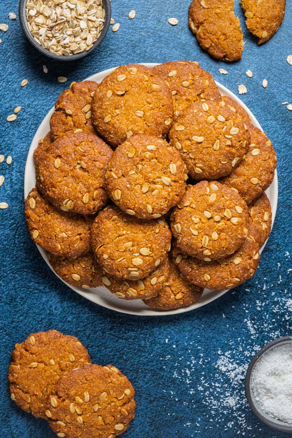 Vegan anzac biscuits stacked up on a white plate. 