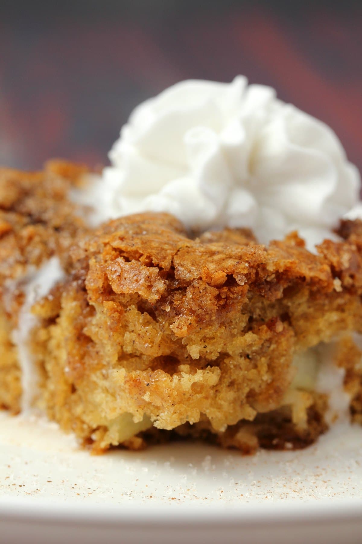 Slice of vegan apple cake topped with vegan whipped cream on a white plate. 