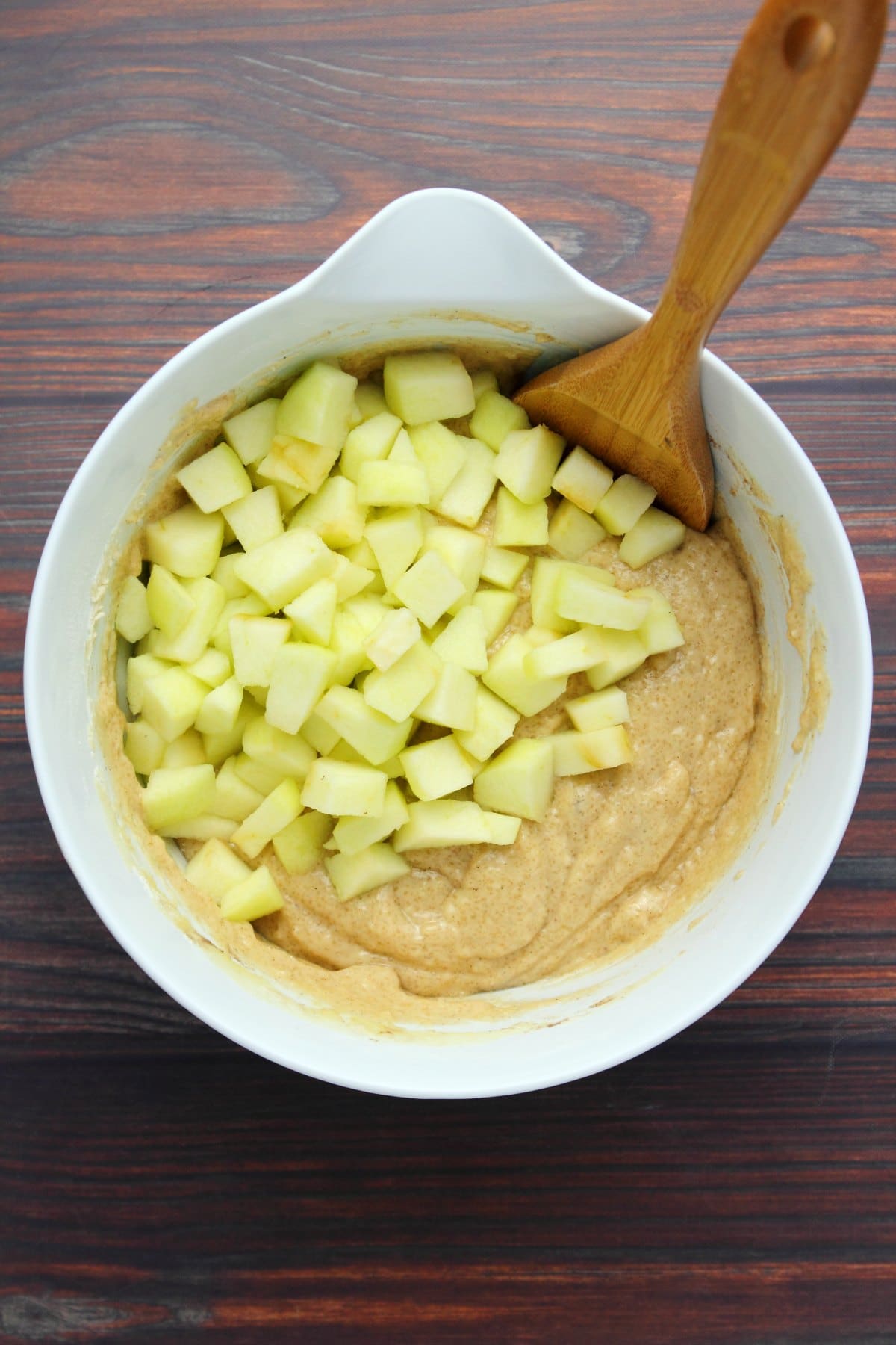 Chopped apple slices on top of vegan apple cake batter in a white mixing bowl. 