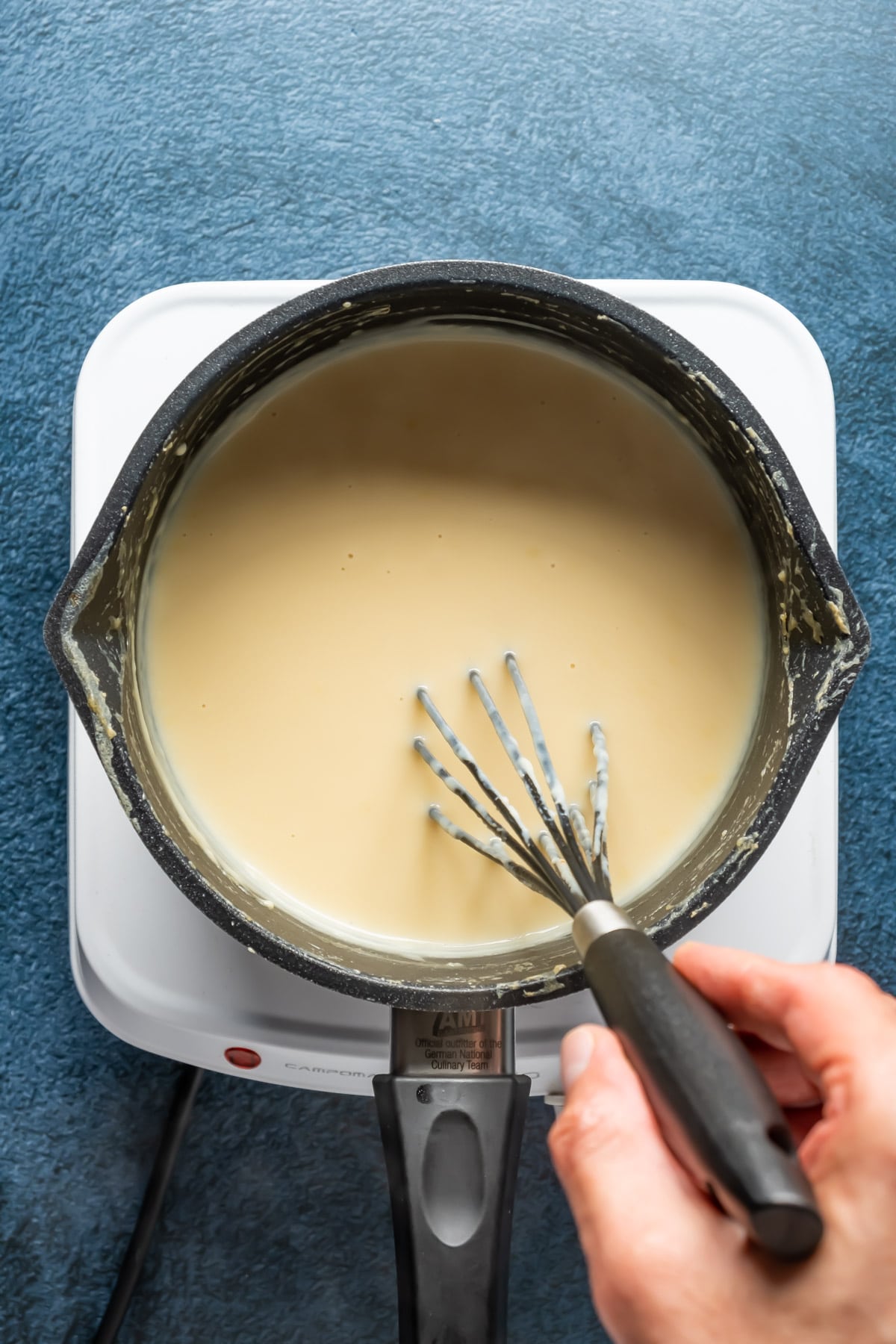Vegan cheese sauce in a saucepan with a whisk.