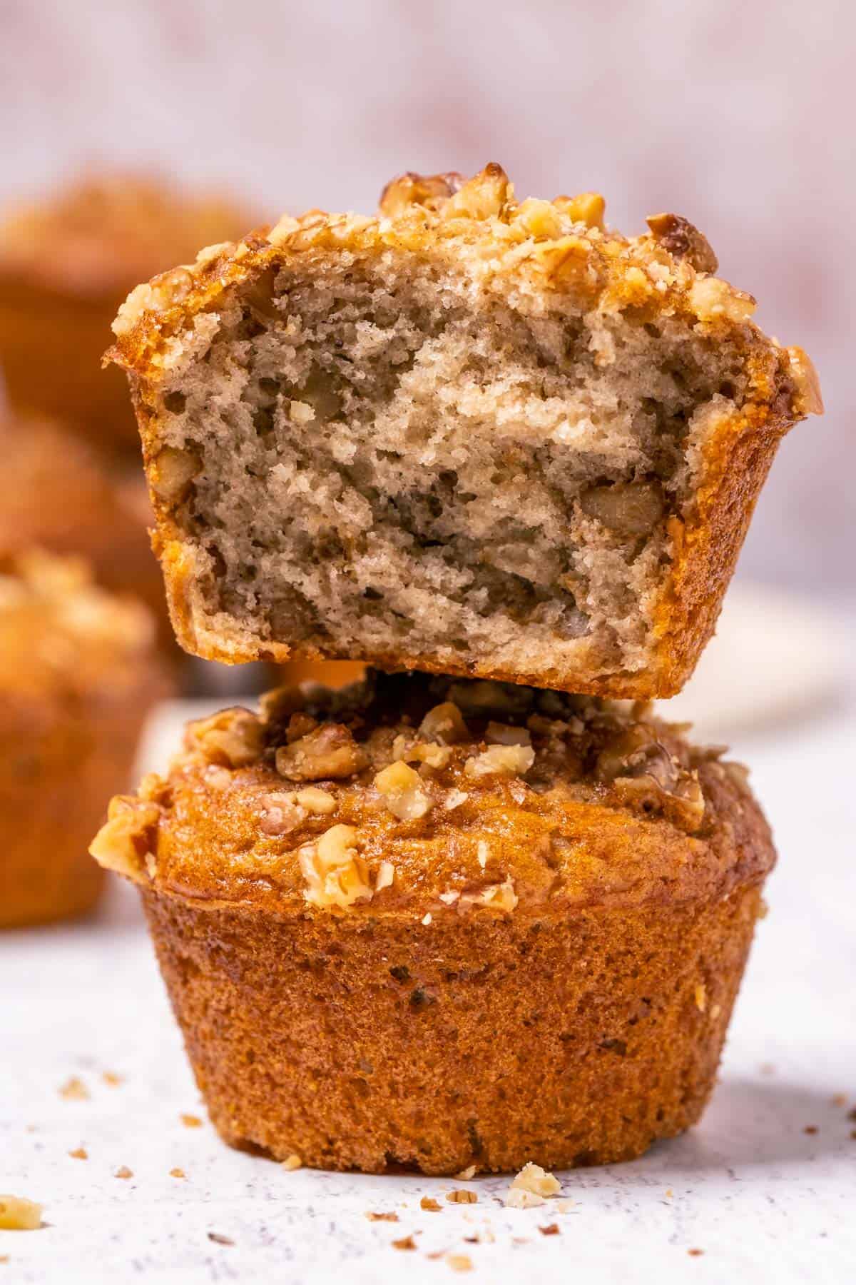 Stack of two vegan banana bread muffins with the top muffin broken in half.