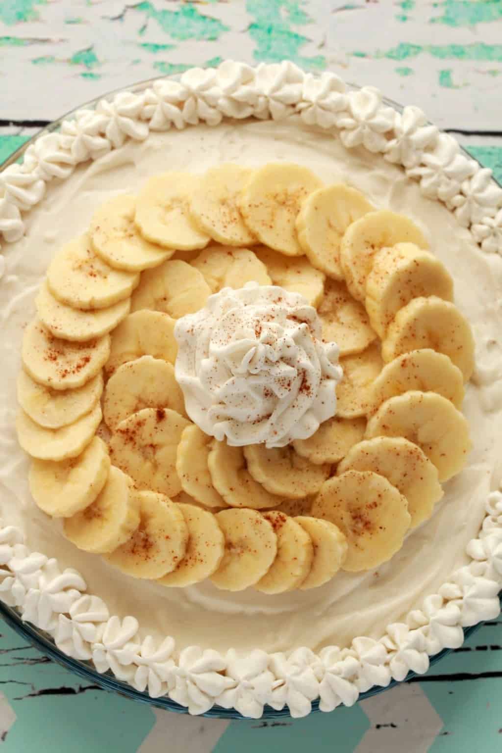 Vegan banana cream pie topped with sliced banana and vegan whipped cream in a glass pie dish. 