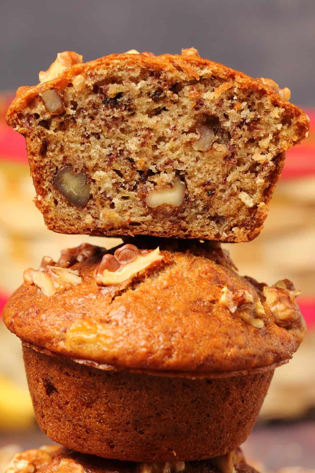 Vegan banana muffins stacked up on top of each other with the top muffin cut in half to show the center. 