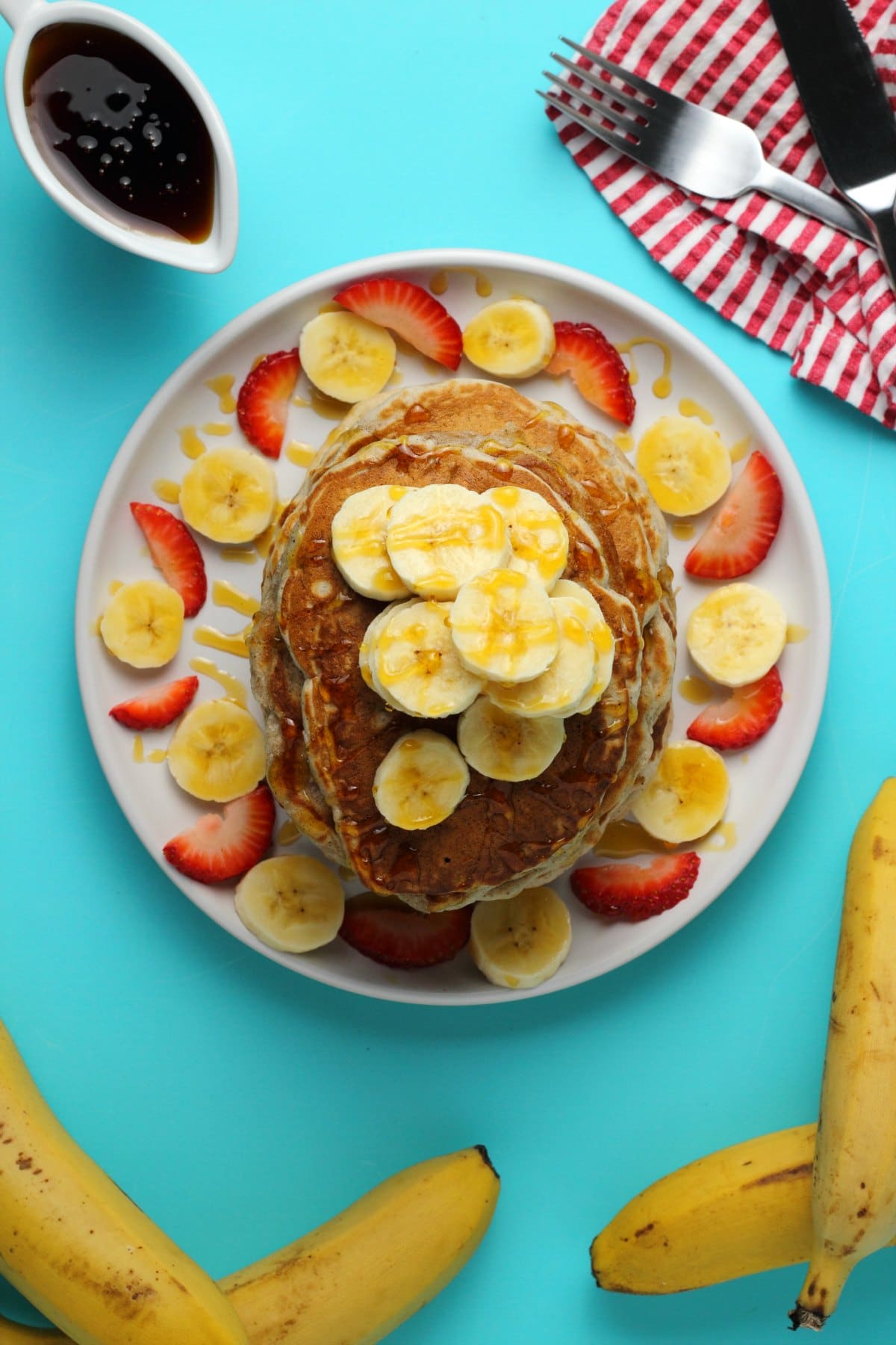 A stack of pancakes topped with sliced banana and drizzled with syrup on a white plate. 