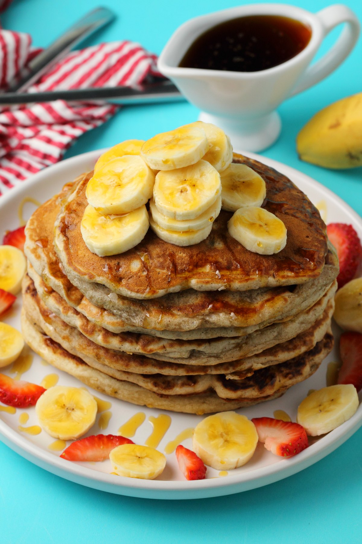 A stack of pancakes topped with sliced banana on a white plate. 