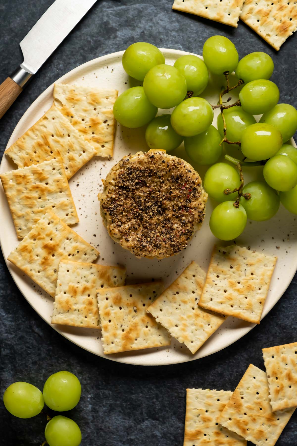 Vegan camembert on a white plate with crackers and grapes. 