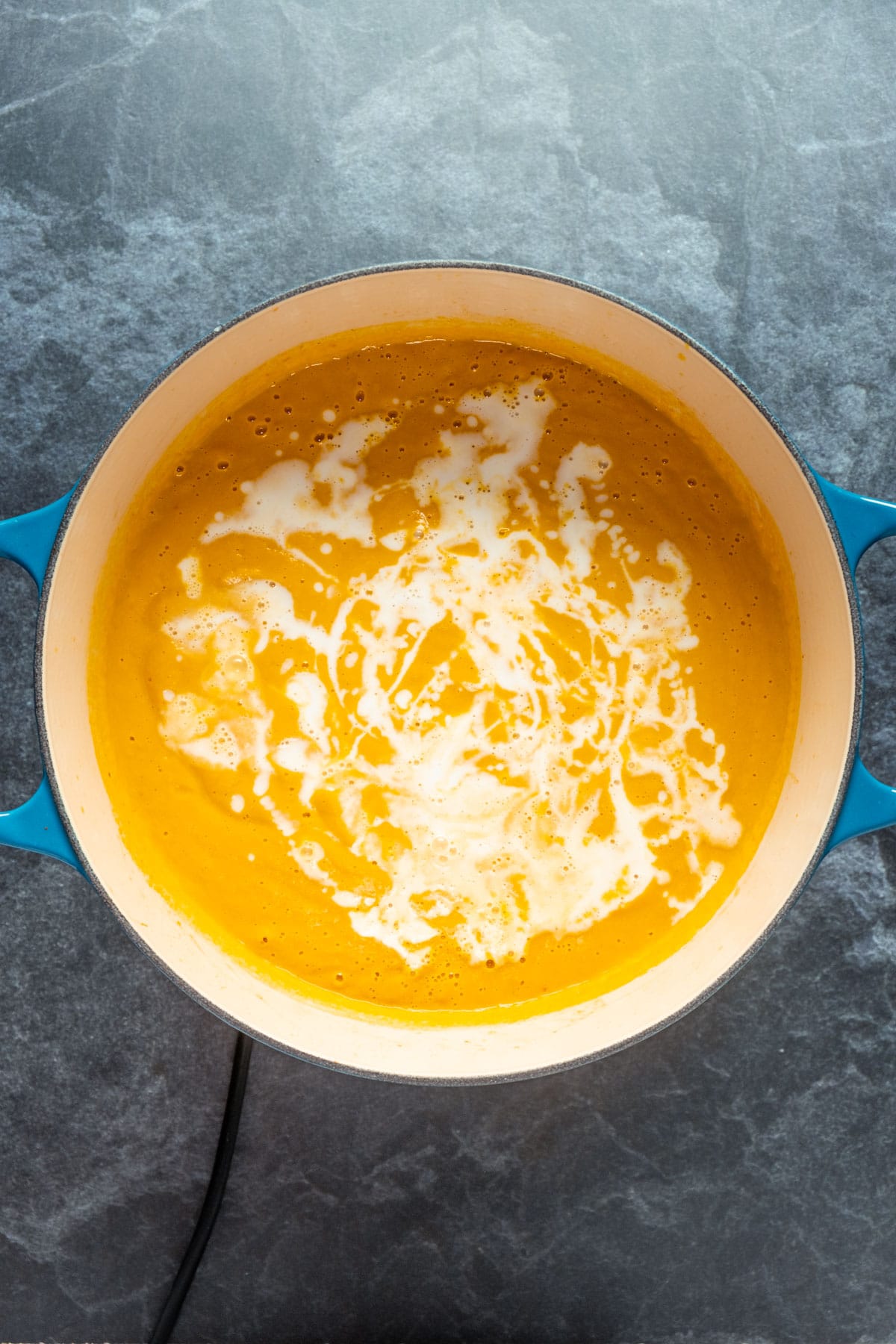 Coconut milk added to blended carrot soup in pot.