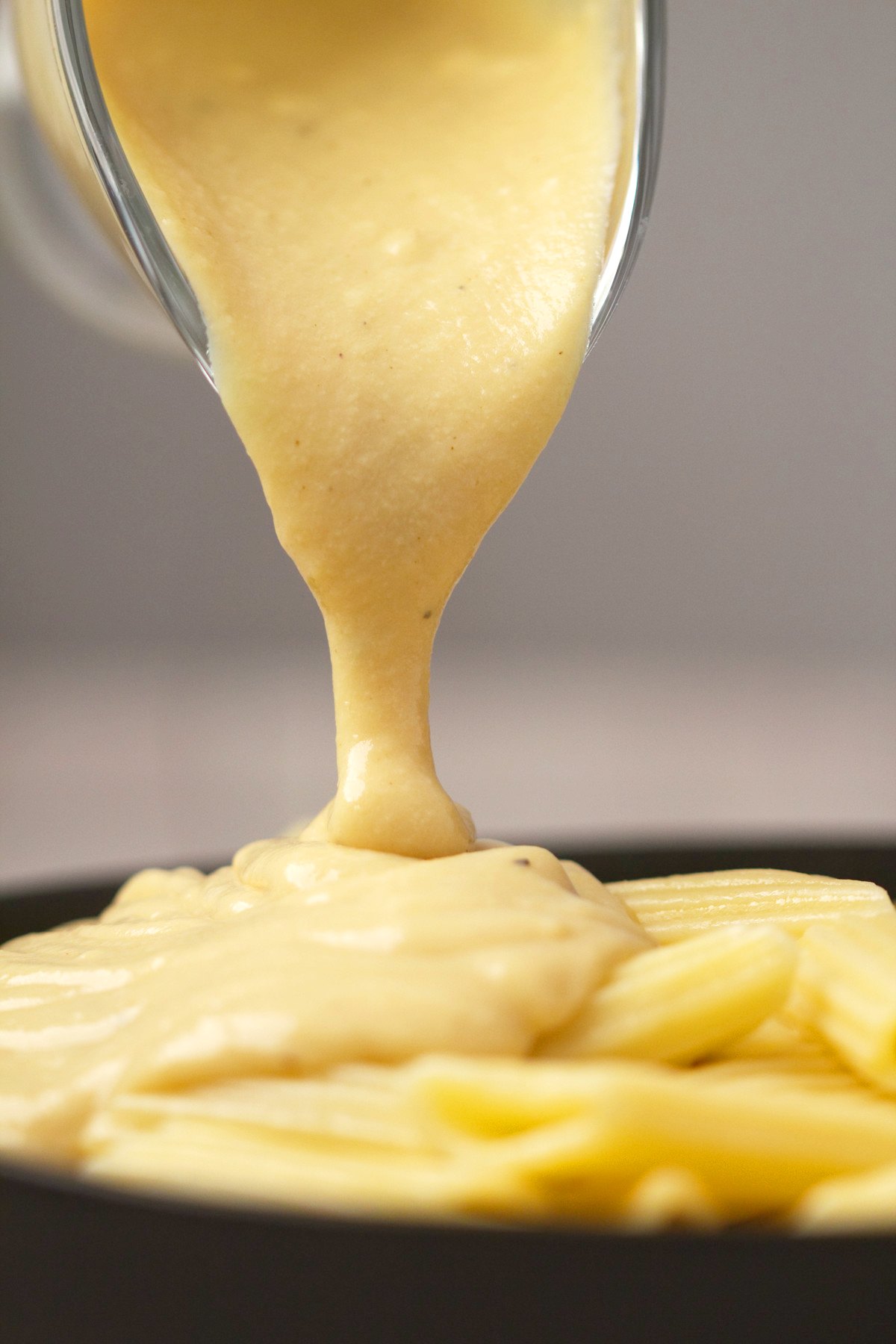 Vegan cheese sauce pouring out over a bowl of pasta. 