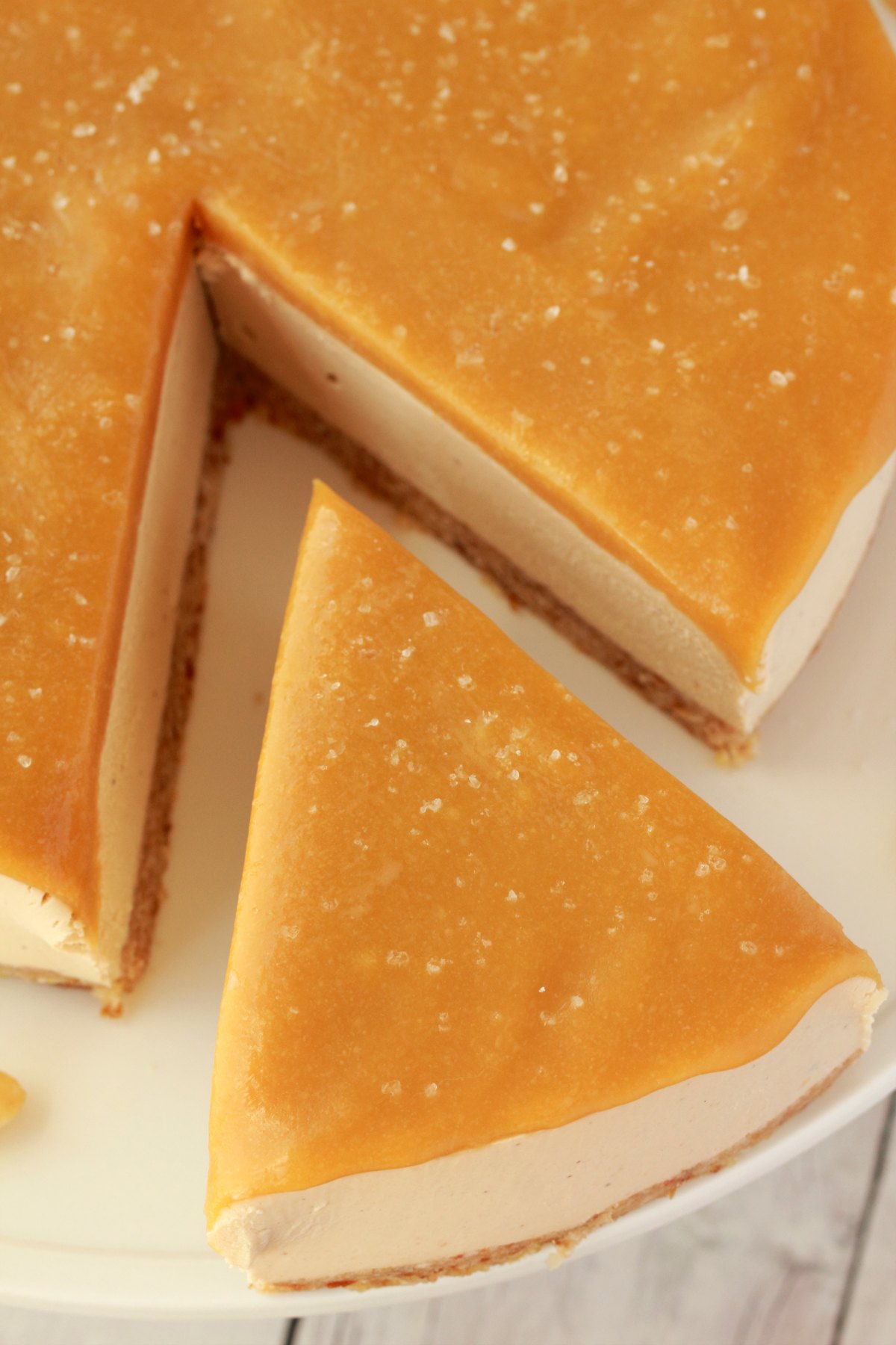 Overhead shot of cheesecake on a white cake stand with one slice cut and ready to be served. 