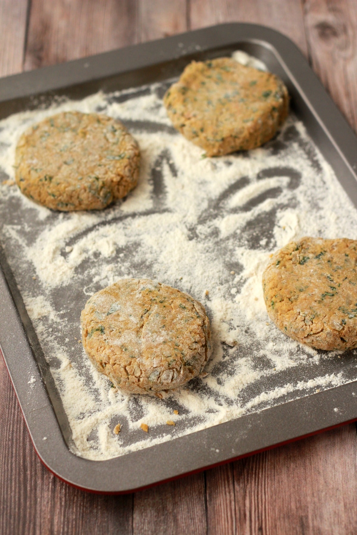 Uncooked vegan chickpea burgers on a flour dusted baking tray. 