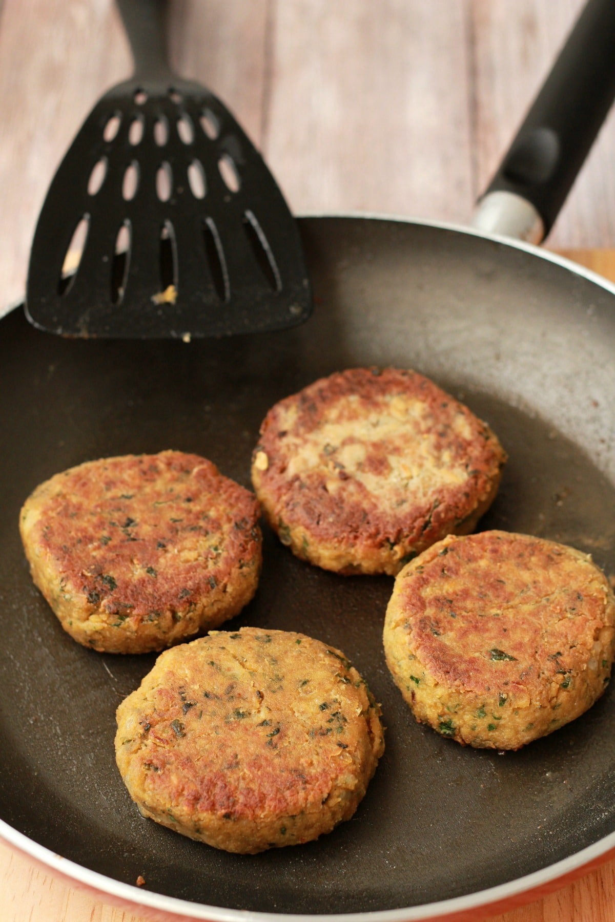 Vegan chickpea burgers nicely browned in a frying pan with a spatula. 