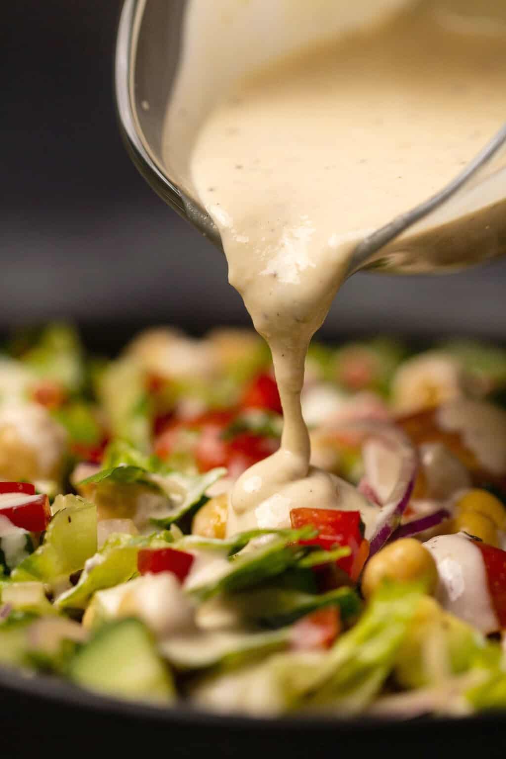 Tahini salad dressing pouring onto a bowl of chickpea salad. 