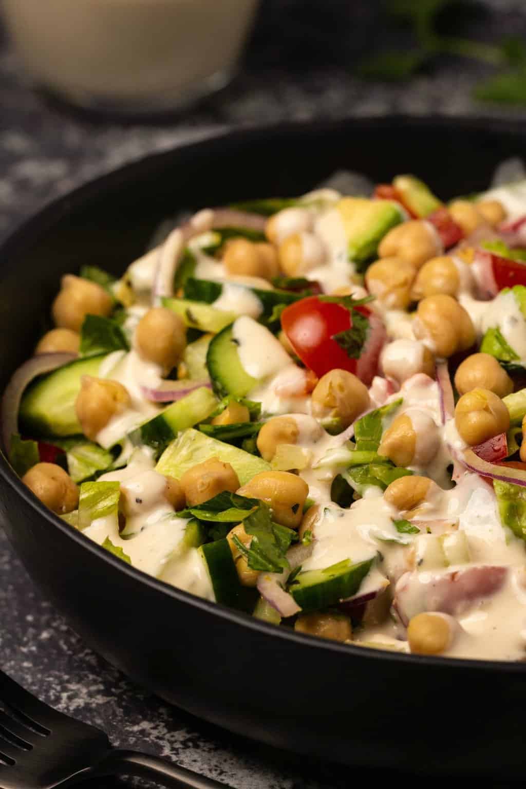Vegan chickpea salad topped with tahini dressing in a black bowl. 