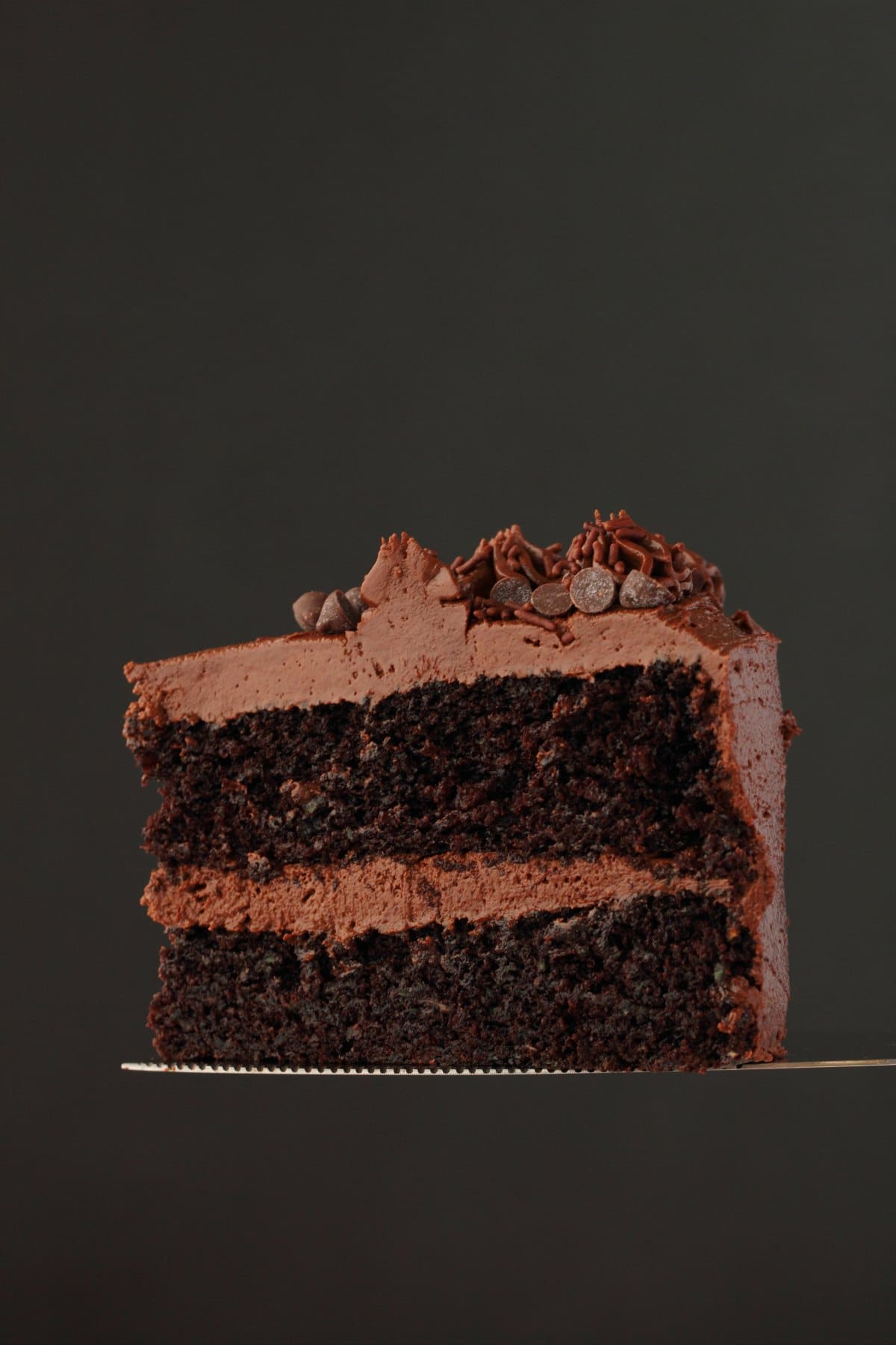 A slice of vegan chocolate zucchini cake on a cake lifter. 