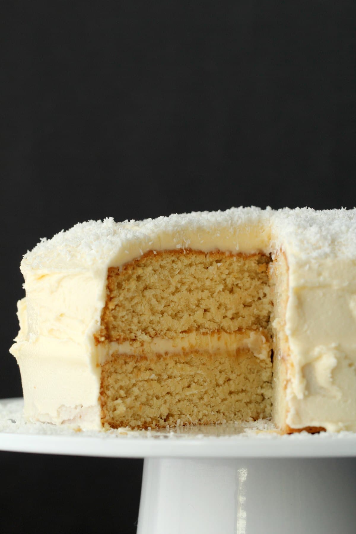 Coconut cake on a white cake stand with one slice missing showing the inside of the cake. 