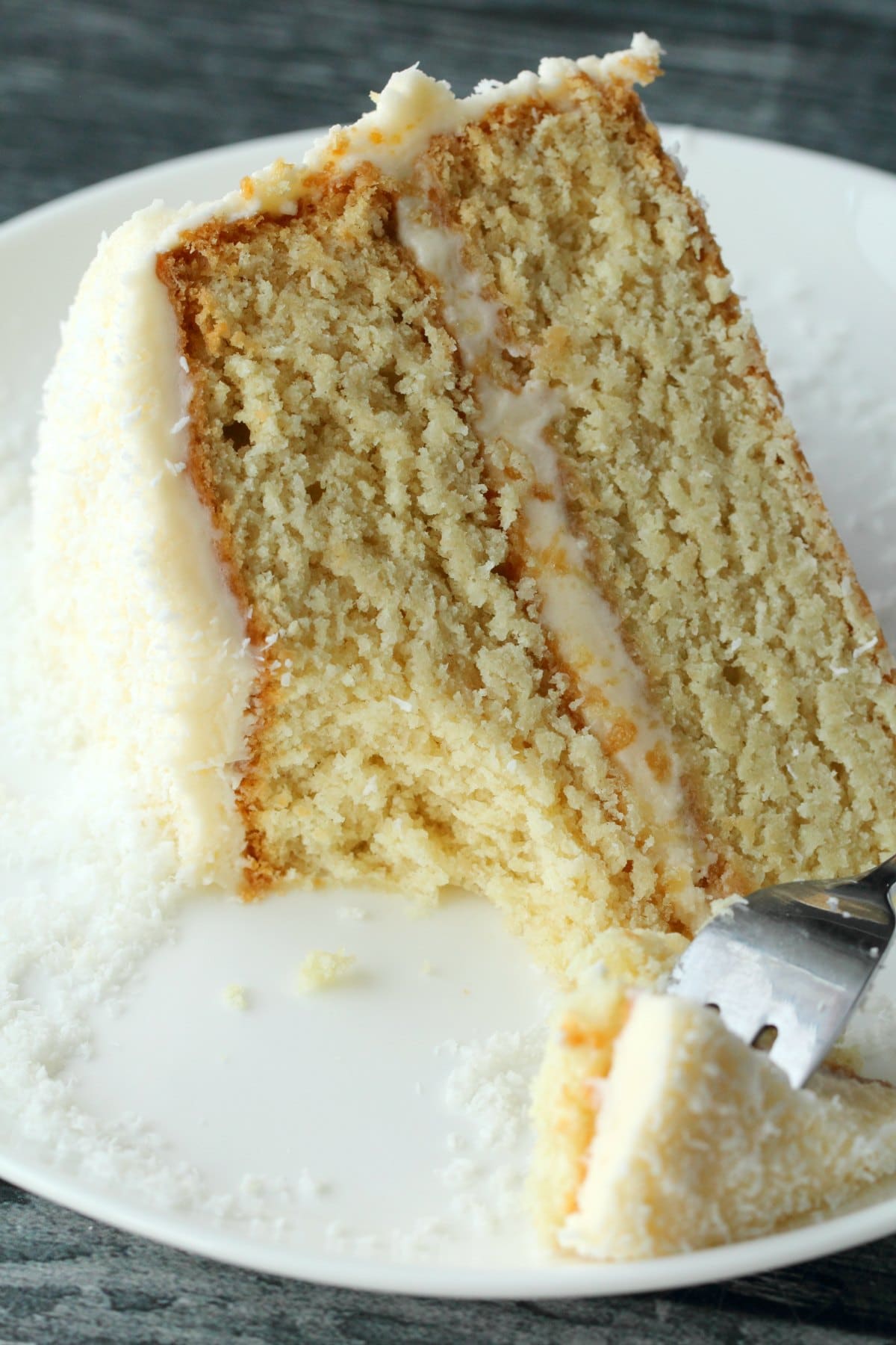 A slice of vegan coconut cake on a white plate with a cake fork. 