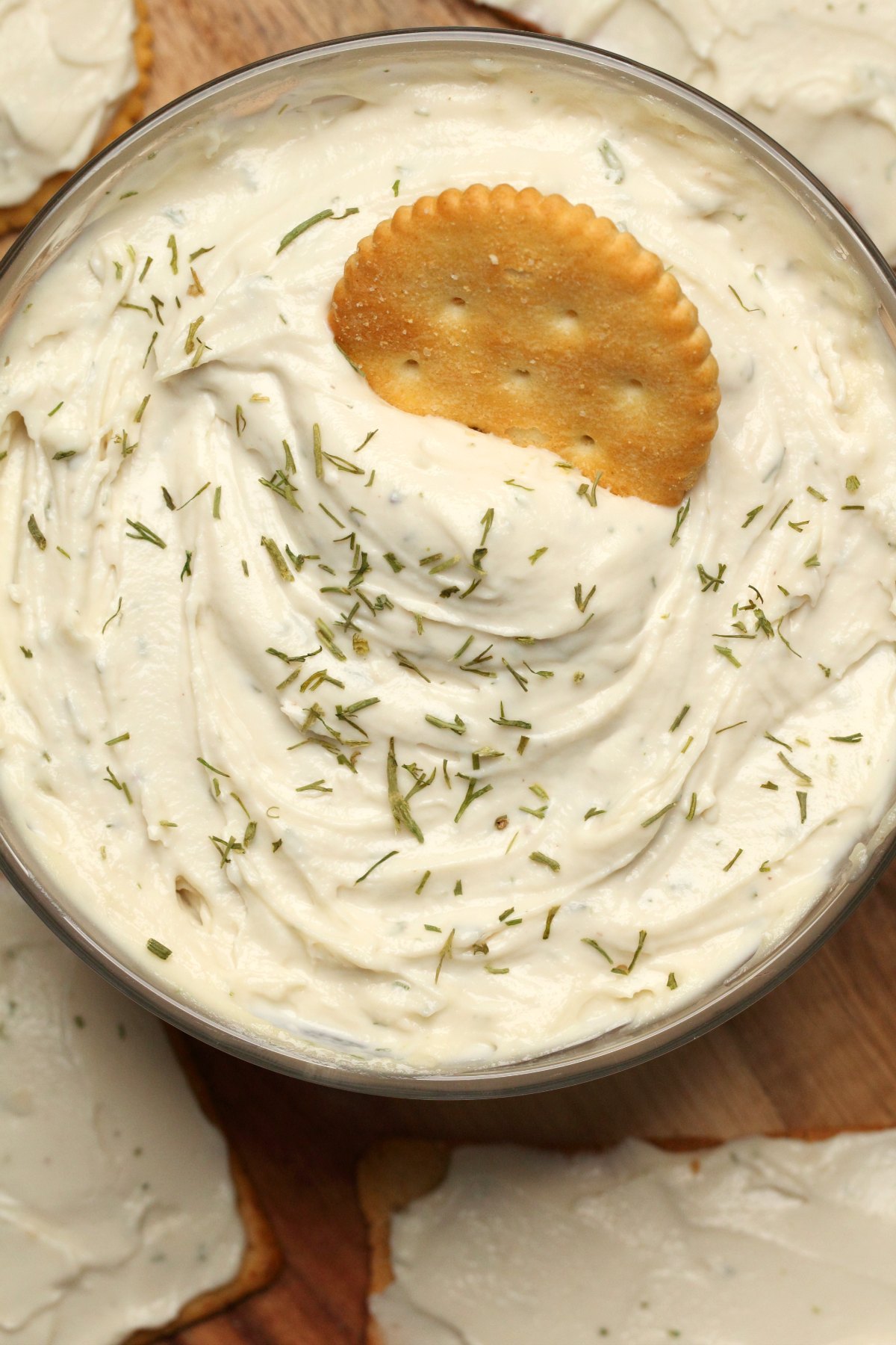 Vegan cream cheese in a glass bowl with a cracker dipping into it. 