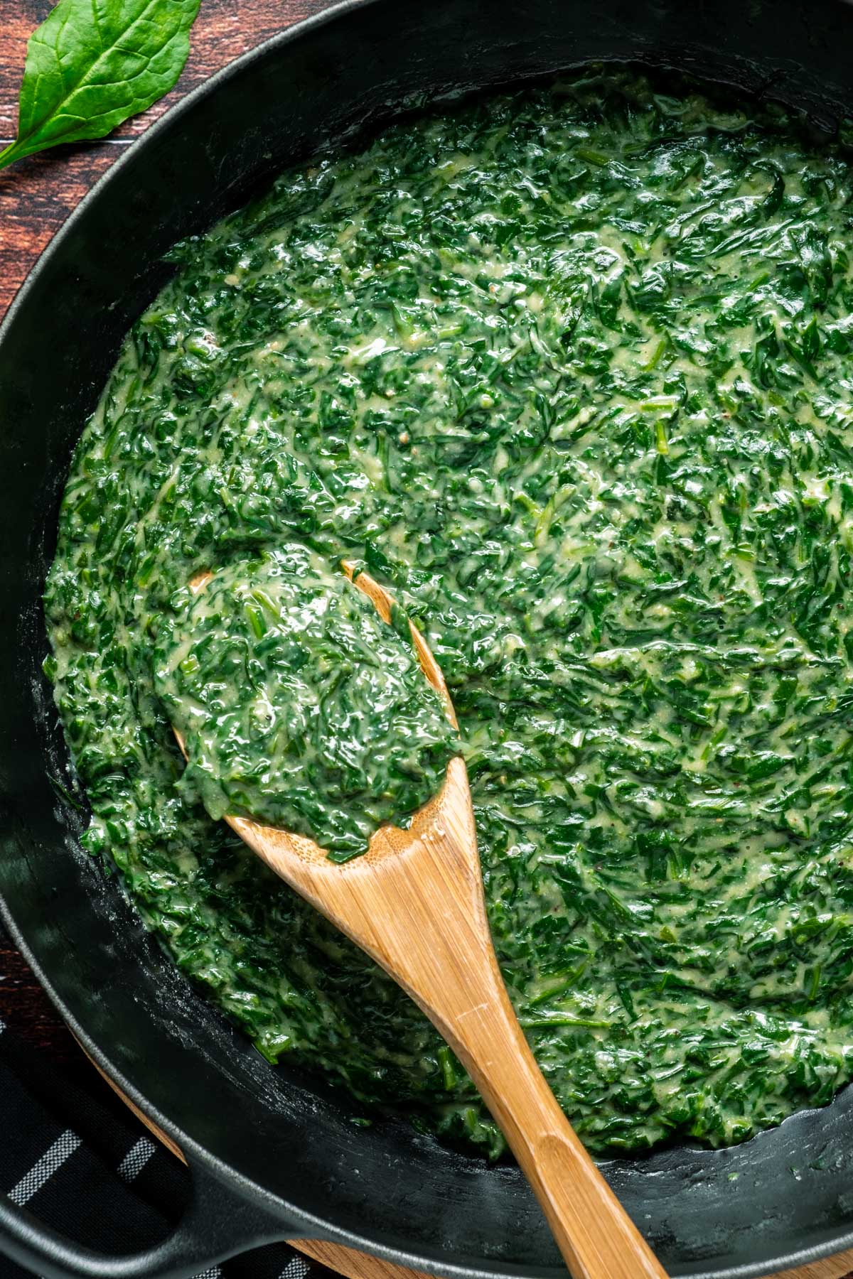 Vegan creamed spinach in a skillet with a wooden spoon.