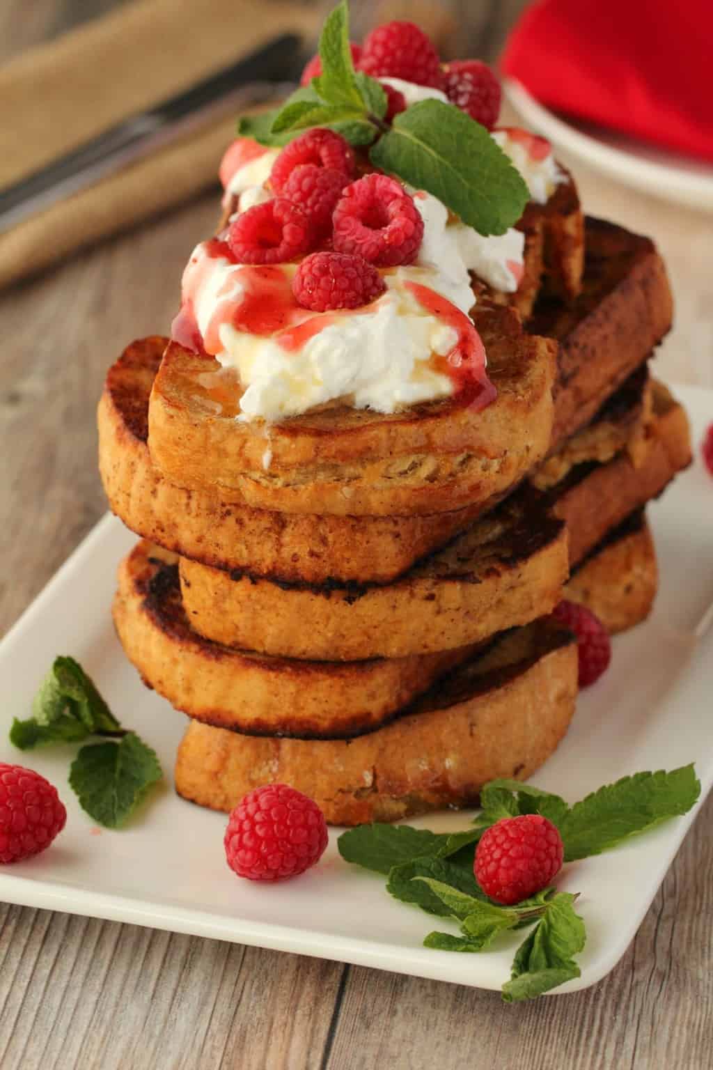 A stack of vegan french toast topped with vegan whipped cream and fresh raspberries. 