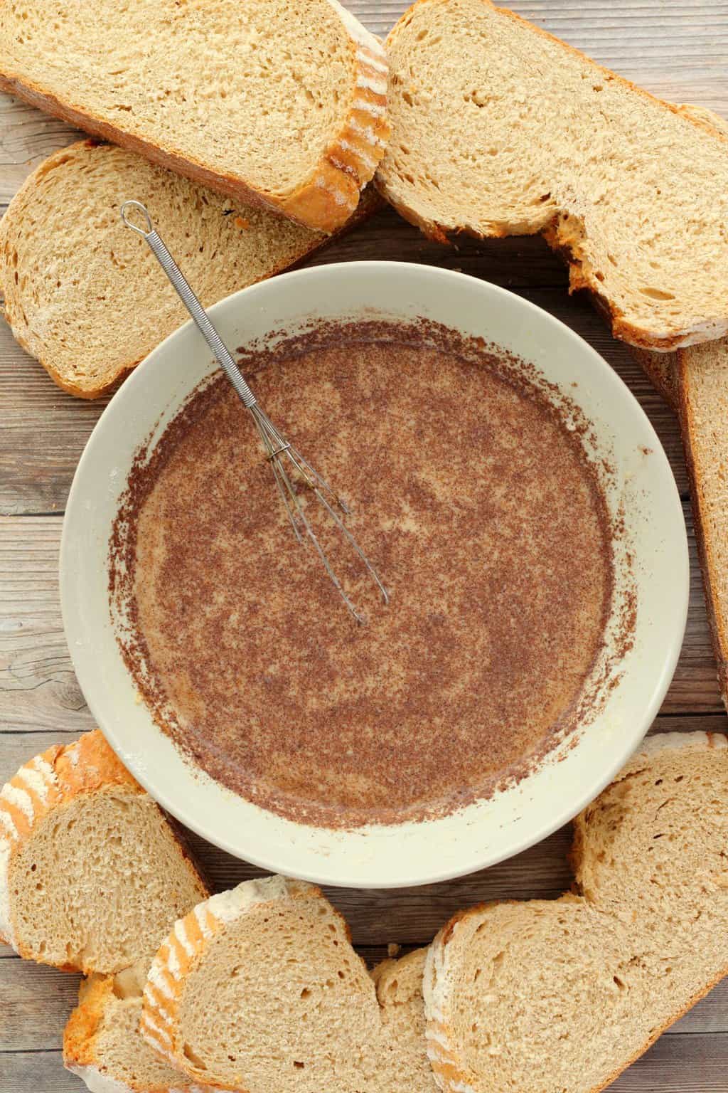 A bowl with the dipping mix for vegan french toast, surrounded by slices of sourdough bread. 