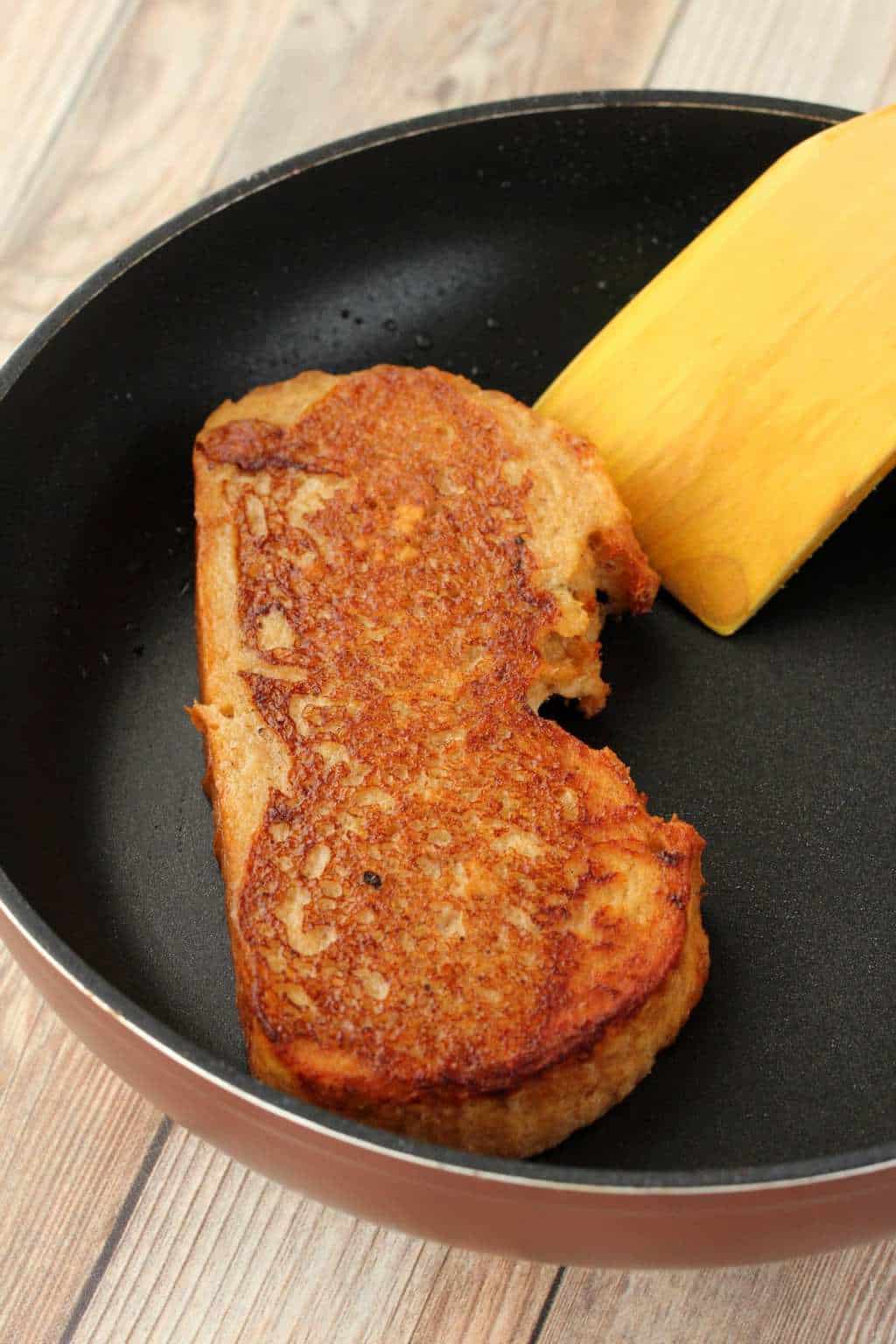 A slice of vegan french toast in a frying pan with a spatula. 
