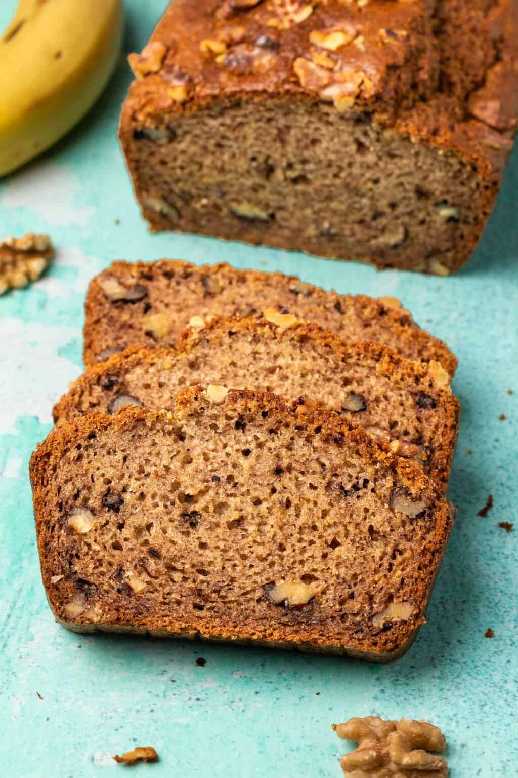 A loaf of vegan gluten free banana bread with 3 cut slices in front of it. 