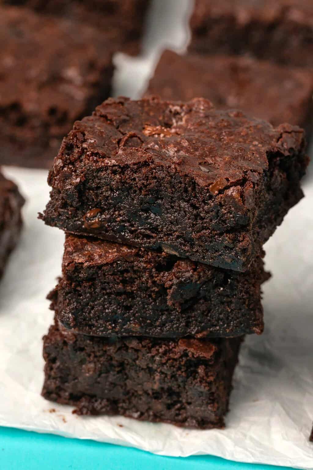 Vegan gluten free brownies stacked up on parchment paper. 