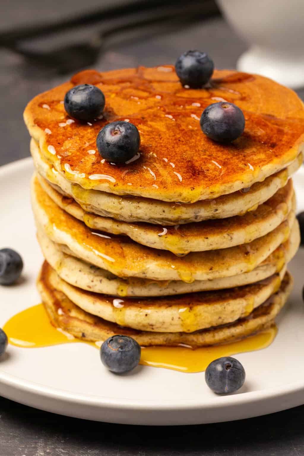 Vegan gluten free pancakes in a stack topped with syrup and fresh blueberries. 
